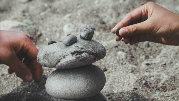 Image of two hands stacking small pebbles on a group of rocks